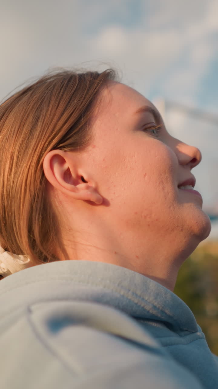 primer plano de una mujer sonriente con suéter azul disfrutando de un juego de voleibol al aire libre, brazos levantados en movimiento con vegetación y edificios en el fondo, bajo la luz del sol brillante