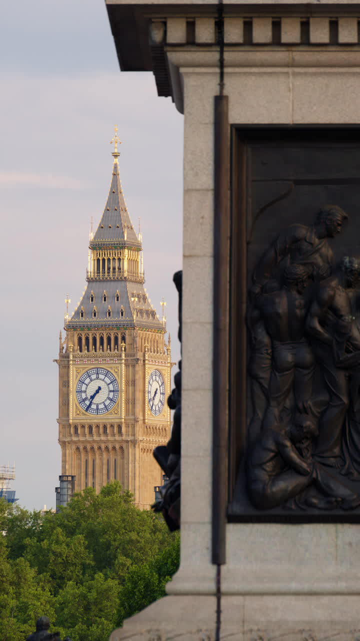 Close-up view of the Big Ben clock tower illuminated by golden sunlight, partly framed by a historic monument in London, England. Vertical