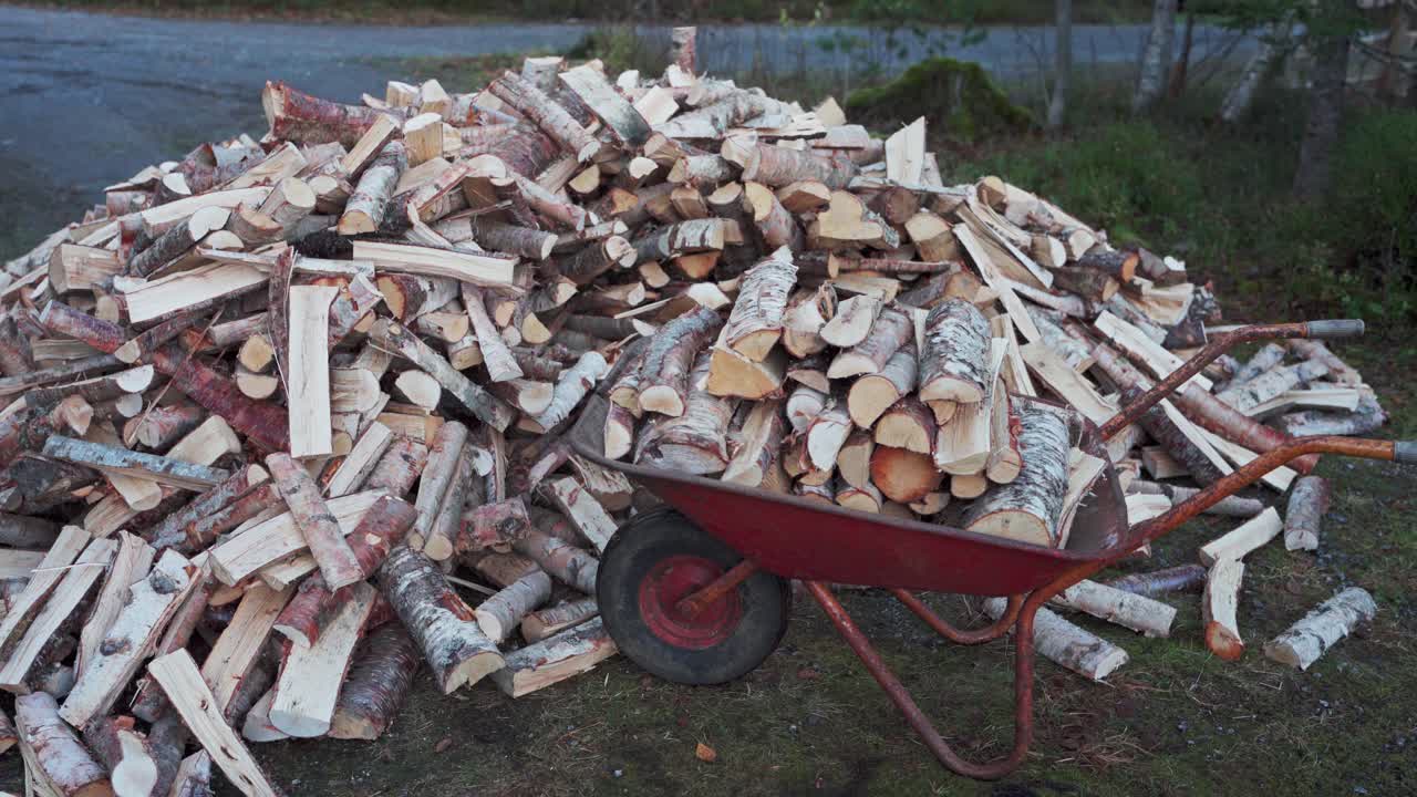 hombre recogiendo leña picada en la carretilla roja