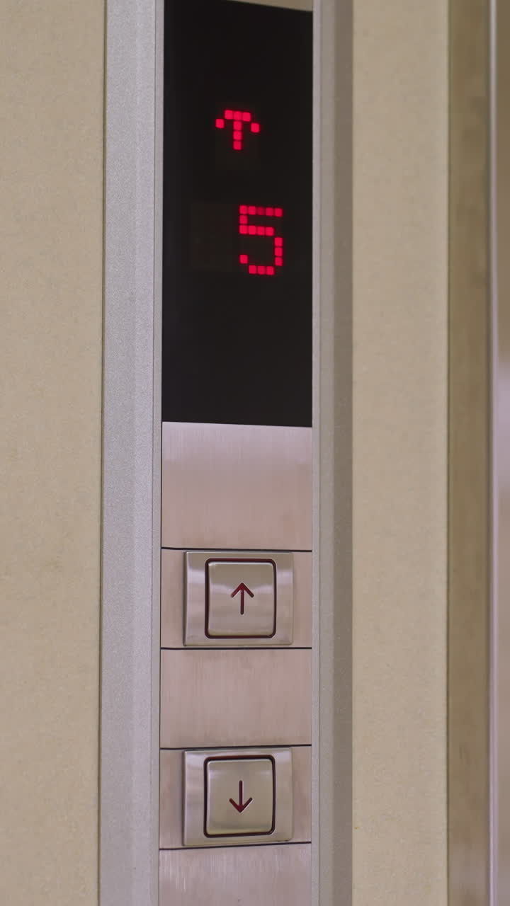 Elevator control panel showing floor 3 with red digits, up and down arrows, and modern design. Smooth, polished metallic finish reflecting elevator functionality and office environment