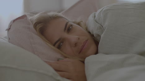 cheerful caucasian woman lying in bed under blanket and smiling