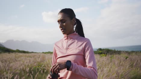 african american woman drinking water from bottle while hiking in the mountains