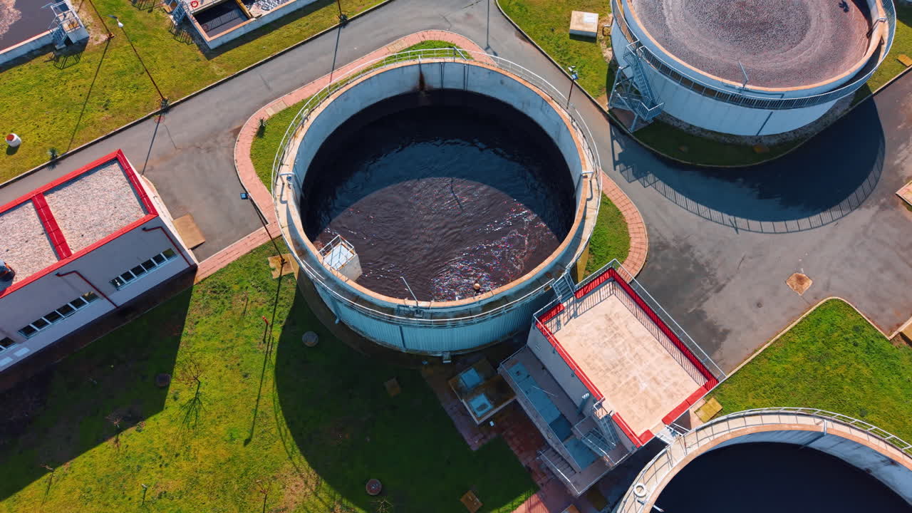Close up aerial view of large circular concrete water tanks. Detailed shot of industrial settling tanks with dark water and surrounding service buildings