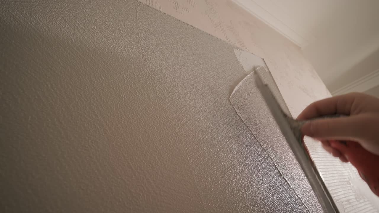 Worker applies decorative plaster with a thin spatula. Giving a unique texture to white walls. Venetian plaster