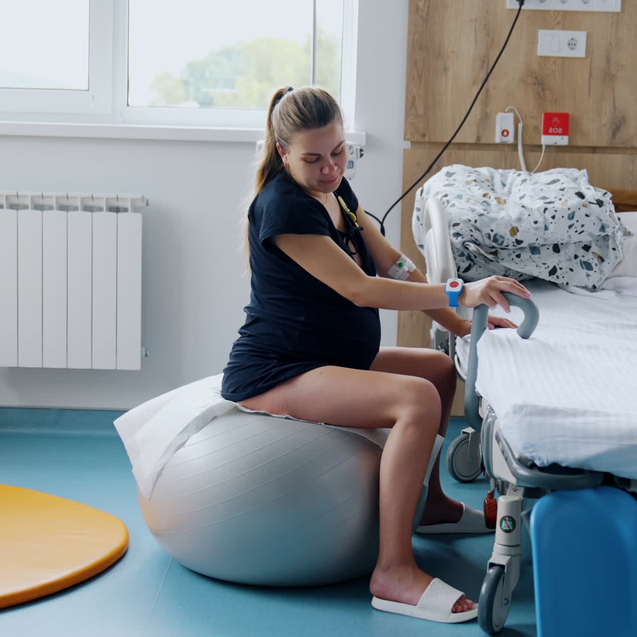 Pregnant woman sitting on the fitball during contractions. Lady moves back and forth to relief pain