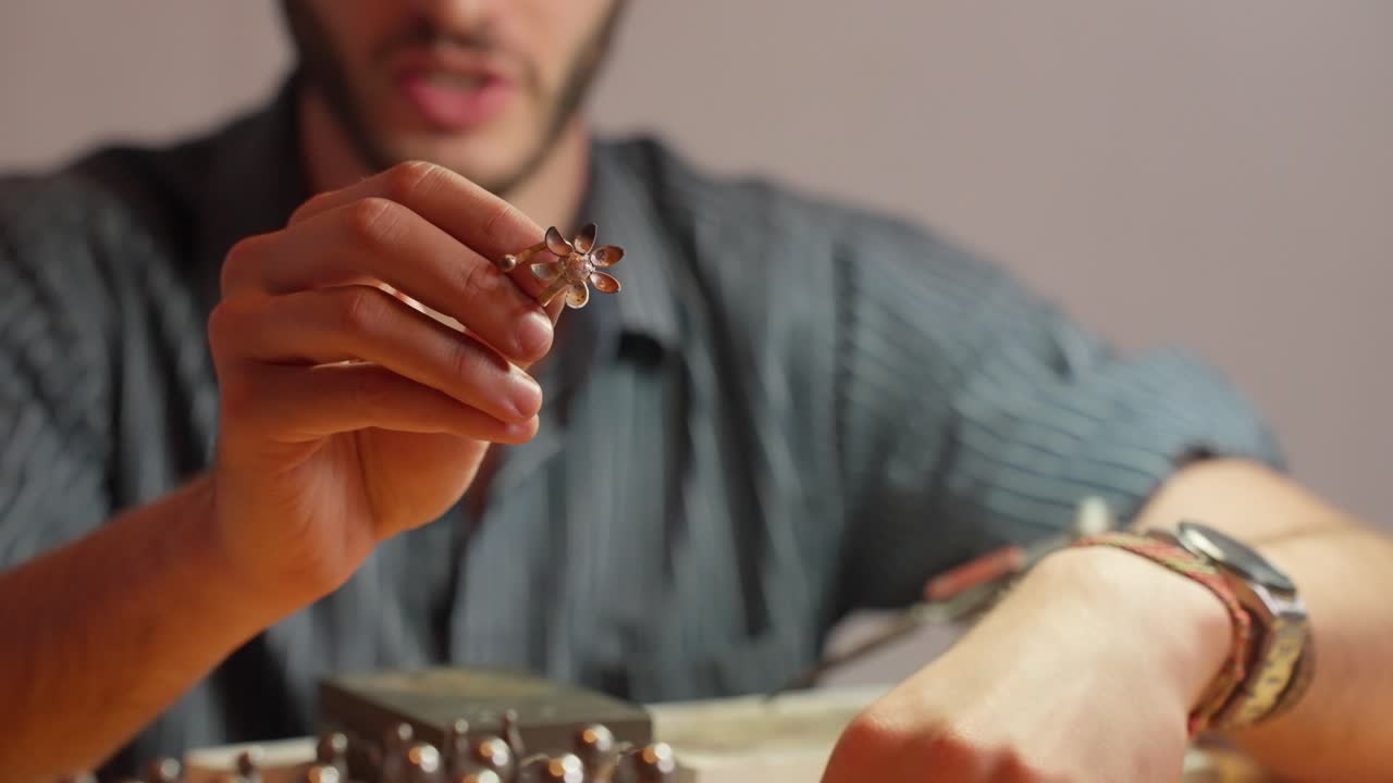 un joven artesano se centra en una pieza decorativa, sosteniéndola en su mano en un taller bien iluminado con herramientas y materiales.