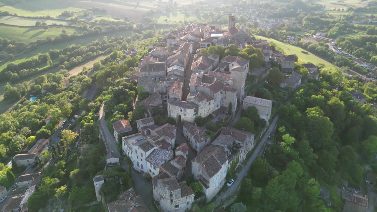 Vista aerea con drone nella campagna francese di una piccola e antica città medievale in mattoni sulla cima di una montagna, circondata da campi verdi, sorvolata in una giornata di sole a Cordes-sur-Ciel