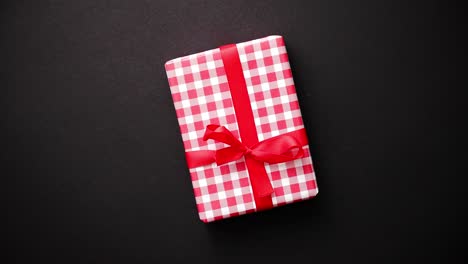 Red-gift-box-with-red-bow-on-black-table--top-view