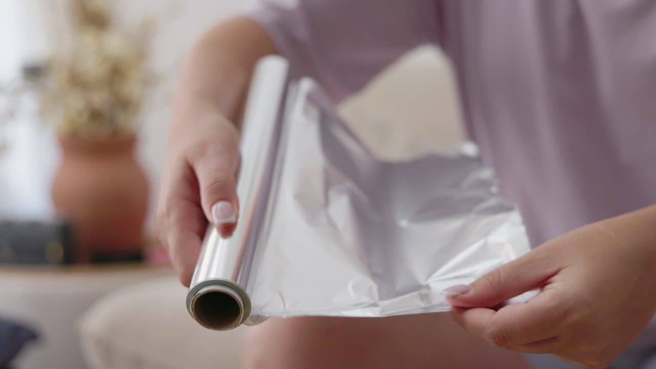 Frau reißt ein Blatt Alufolie von der Küchenrolle zum Kochen ab.
