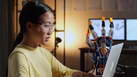 close up of teen asian girl thinking while working about a cyborg hand on a laptop at home