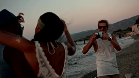 amigos multiétnicos tomando fotos de vacaciones con una cámara vintage en la playa