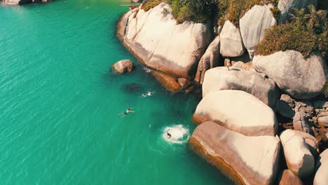 female jumping from a big rock into the clear water sea on a summer sunny day