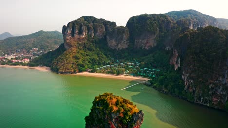 drone flies over a limestone cliff to reveal a beachfront resort at railay beach, krabi. turquoise waters and lush greenery make this scene ideal for travel and tourism content.