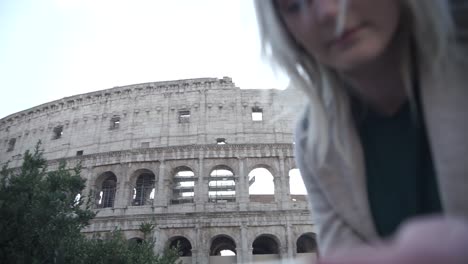 a blonde girl playing with her phone in front of colloseum