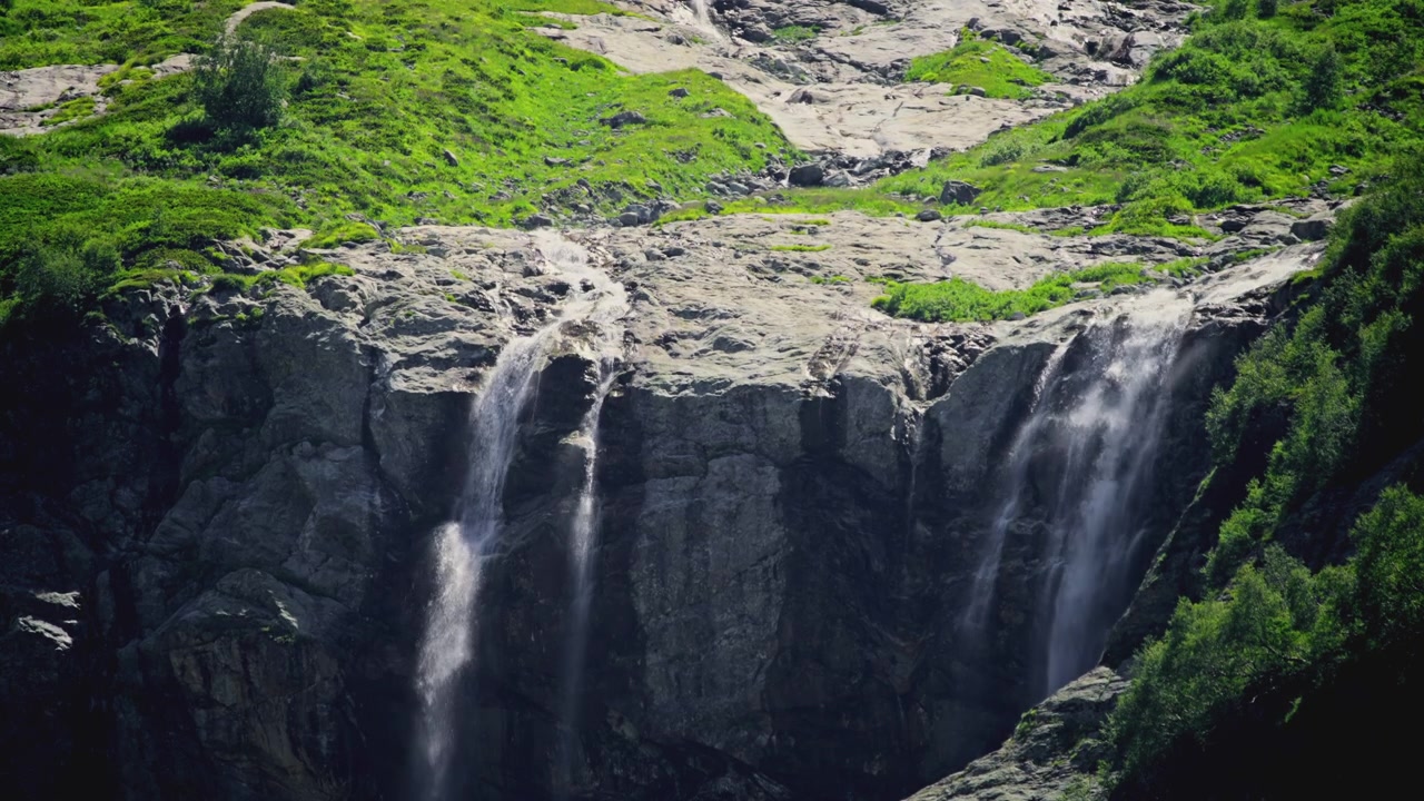 Diverse cascate che scendono a picco da una parete rocciosa di montagna verde