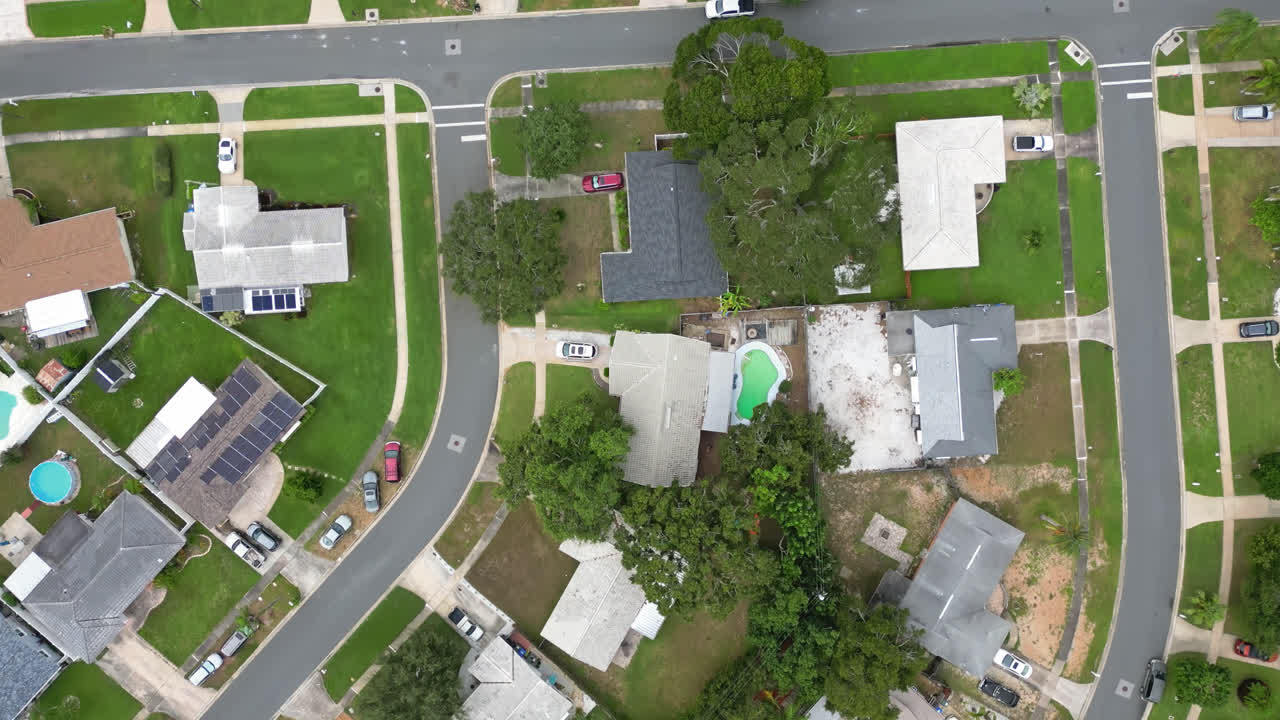 Aerial top down view over suburban neighborhood houses with green grass yards and large trees all over