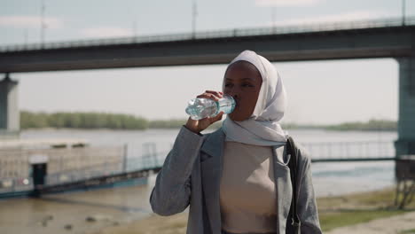 Junge-Schwarze-Arabische-Frau-Trinkt-Wasser-In-Flaschen-Am-Flussufer