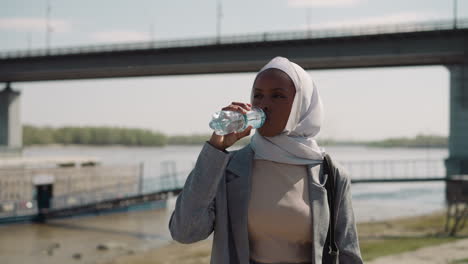 young black arabian woman drinks bottled water at riverside