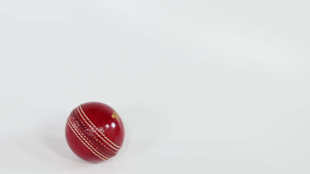 En röd cricketboll i läder kommer in i bildutsnittet, faller och studsar sedan mot en vit bakgrund.