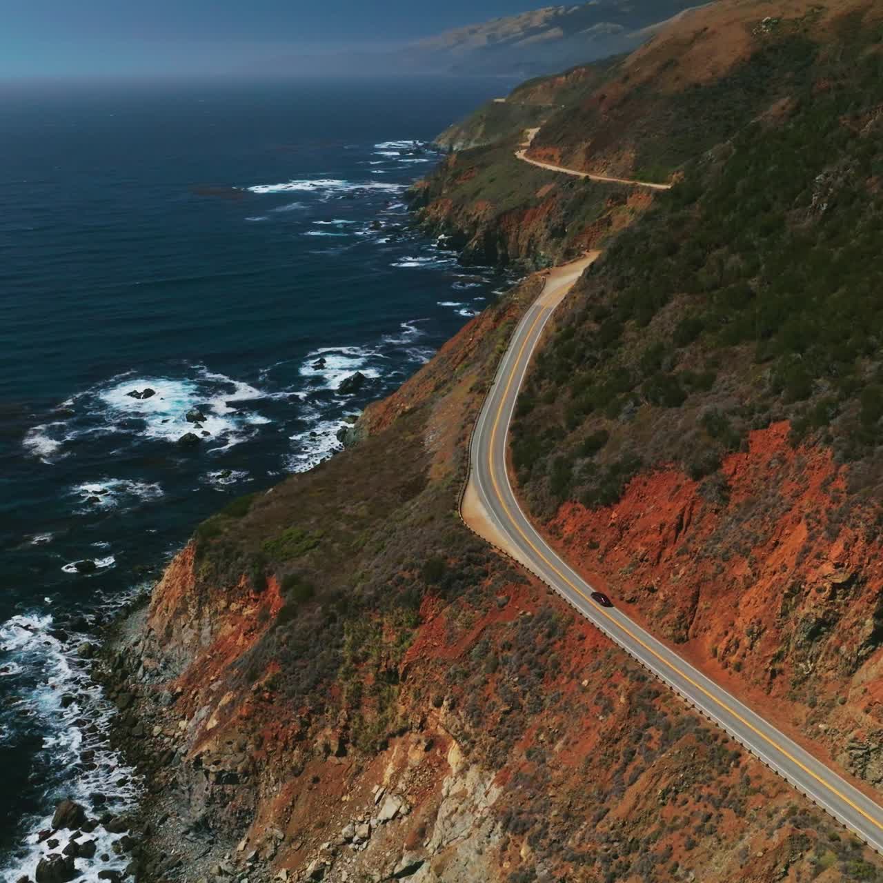 Magnificent mountains of California with highway in the middle. Dark blue ocean with white foamy waves. Aerial perspective