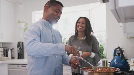 Una-Pareja-Afroamericana-De-Mediana-Edad-Está-Hablando-En-La-Cocina,-Un-Hombre-Preparando-Comida-En-La-Encimera,-Con-La-Cintura-Para-Arriba