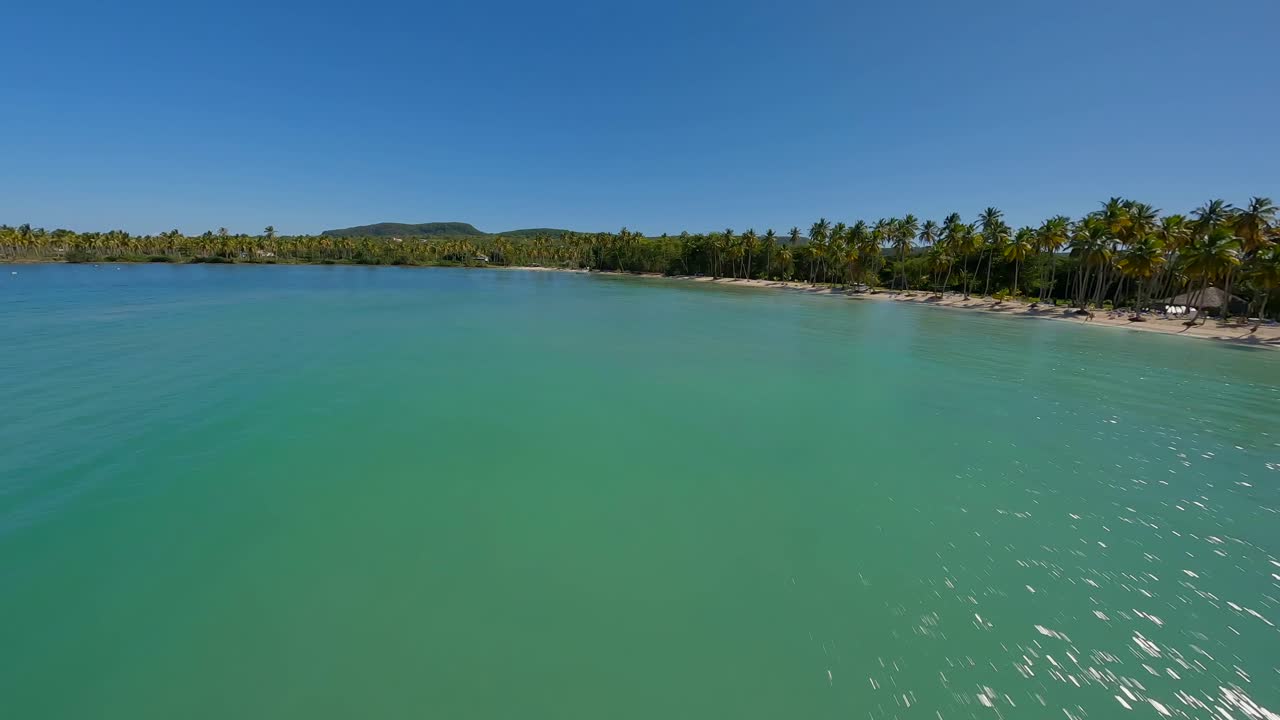 Vista aérea cinematográfica de drone em alta velocidade sobre água verde do oceano com litoral tropical e o brilho do sol
