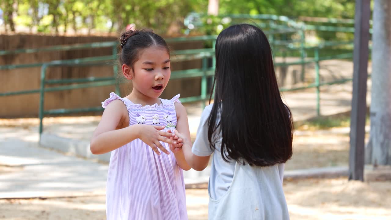 ภาพระยะกลางของเด็กผู้หญิงสองคนกำลังเล่นเกมตบมือกลางแจ้งในเวลากลางวันที่แสงธรรมชาติสดใส