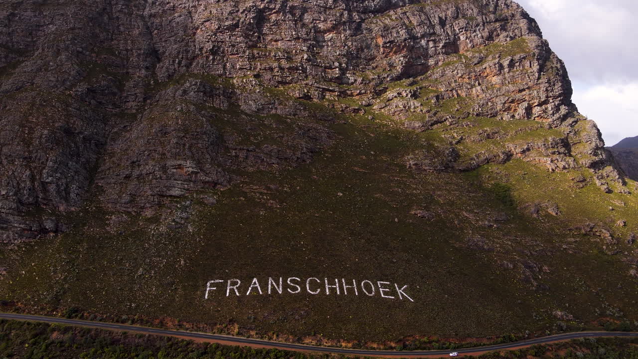 Name of Franschhoek laid out in white stones on rugged mountainside; aerial