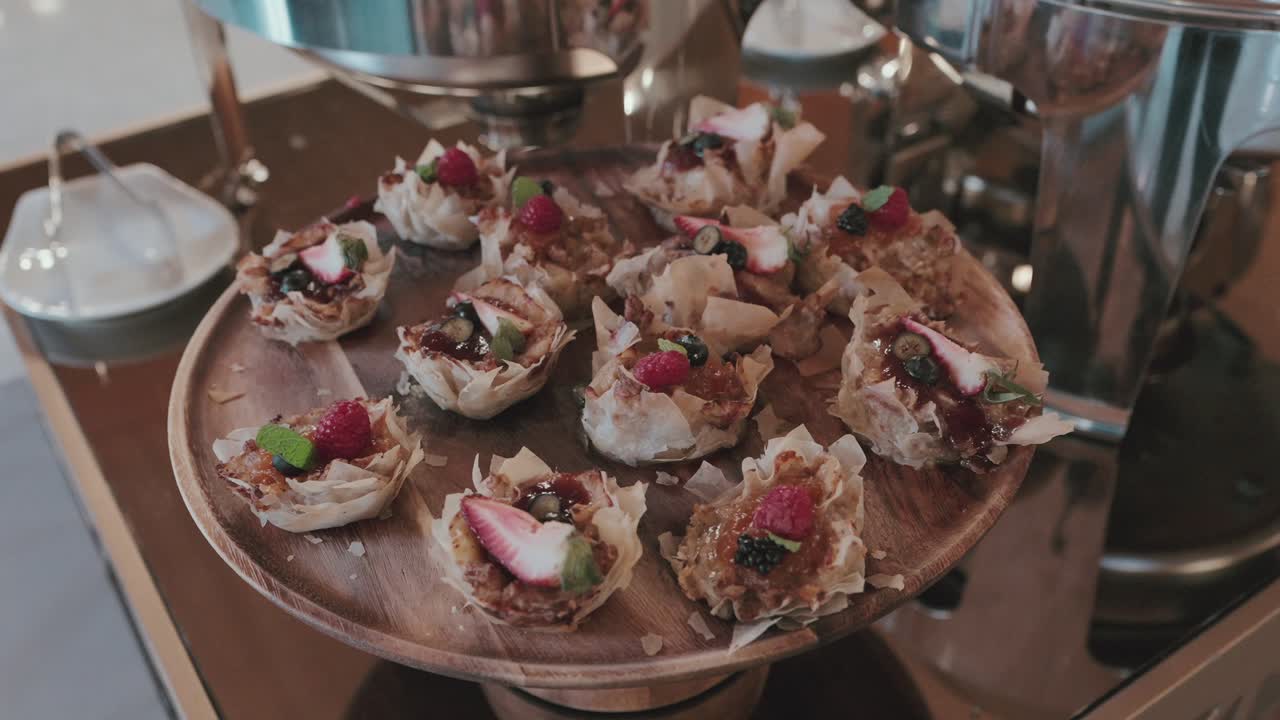 mini filo pastry tartlets topped with assorted berries mint and syrup on wooden dessert stand