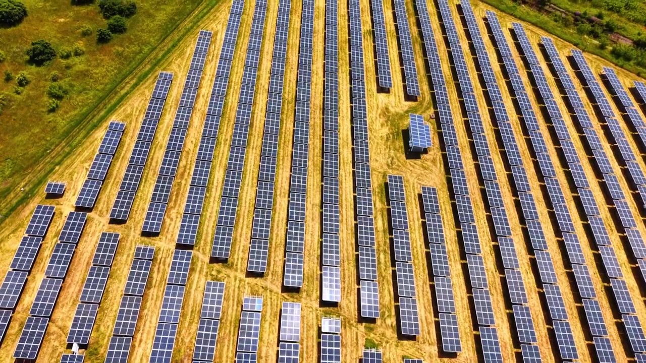 Luftfoto ovenfra af solpaneler på en gylden mark. Dronebillede direkte ovenfra af symmetriske rækker af solpaneler på tør græsklædt jord.