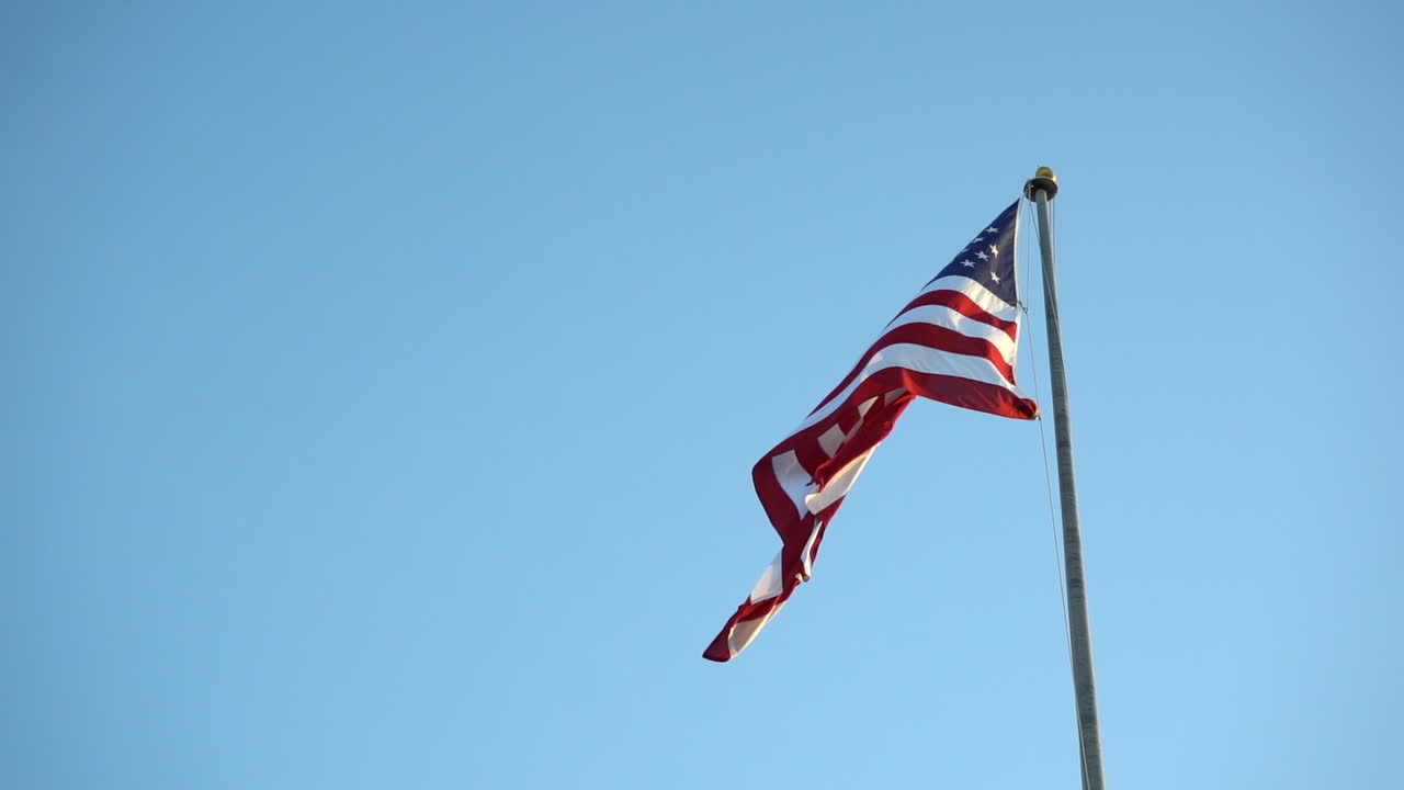 bandera estadounidense en un asta de bandera contra el cielo azul, moviéndose lentamente en el viento