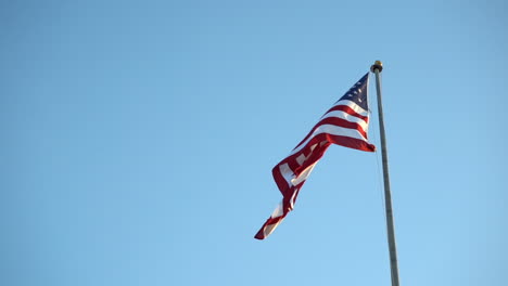 american flag on a flag pole against blue sky, slowly moving in the wind