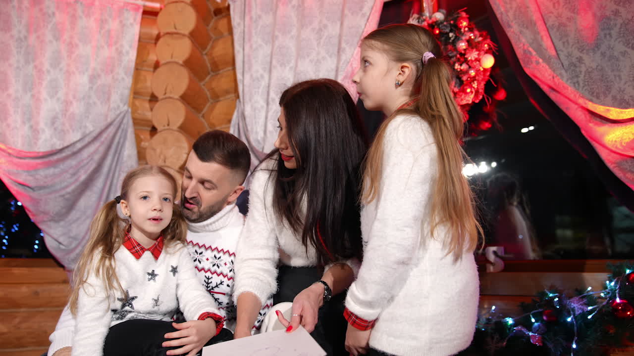Family sitting together in the living-room. Parents speaking with their children at Christmas time. Happy family members in festive sweaters at Christmas night.