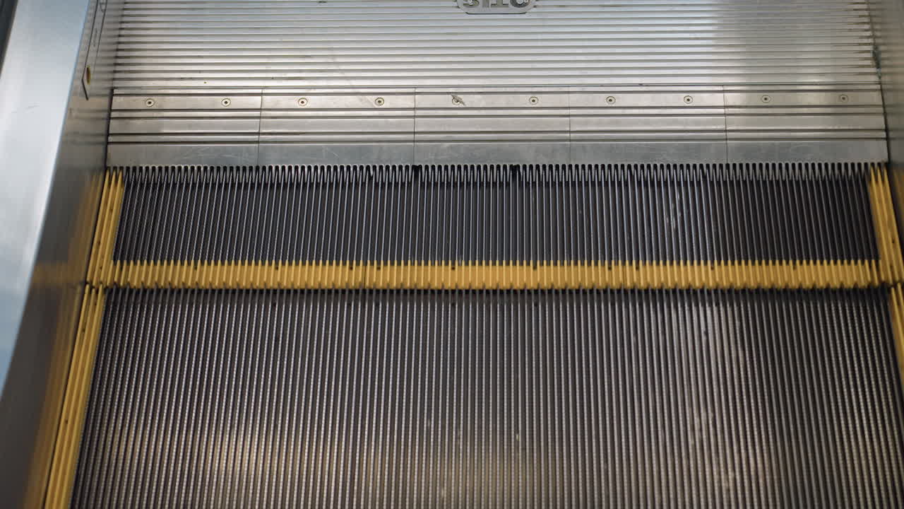 Close up of moving escalator steps with black ridged surface and yellow edge lines in modern shopping mall, showcasing motion, metallic details, and structural design