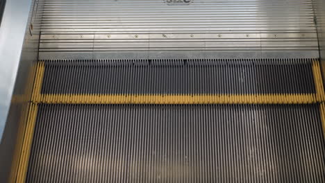 close up of moving escalator steps with black ridged surface and yellow edge lines in modern shopping mall, showcasing motion, metallic details, and structural design
