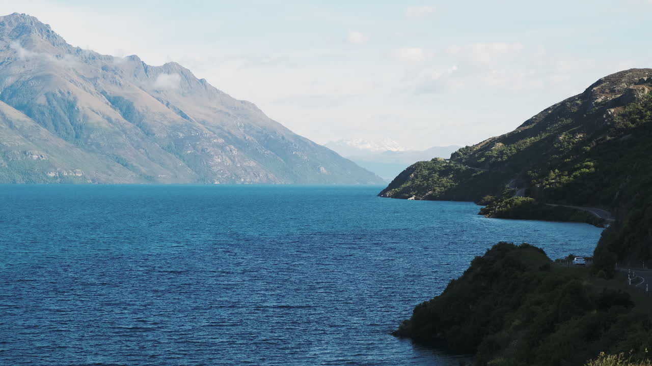 밝은 푸른 호수를 따라 구불구불한 뉴질랜드 산악 도로를 달리는 자동차