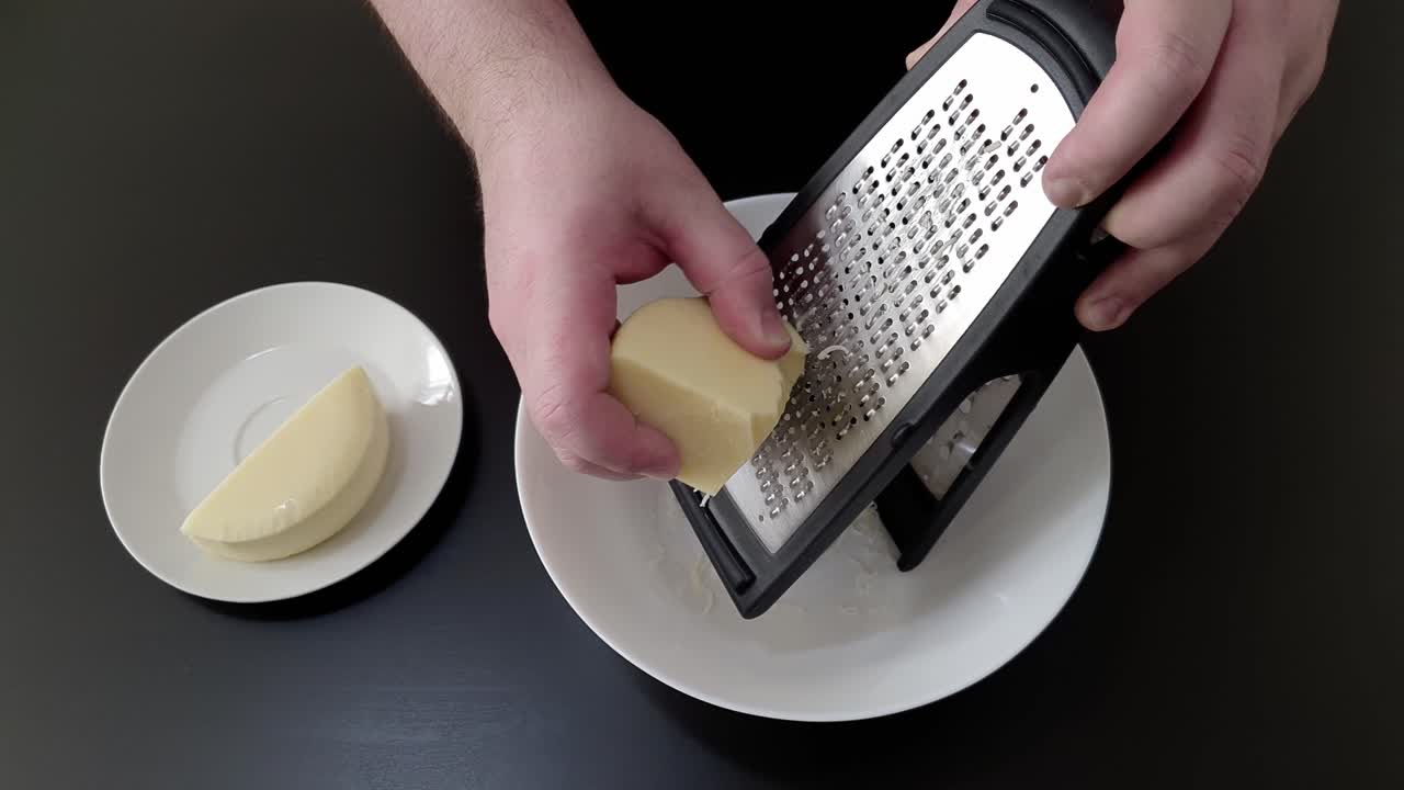 Mani che grattugiano formaggio con una grattugia in un piatto