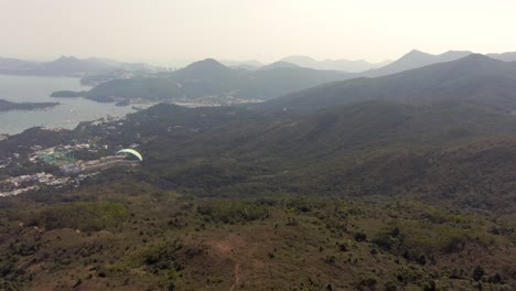 Parapente-Sobre-Las-Montañas-De-Hong-Kong-En-Un-Hermoso-Día-Claro-Con-Rascacielos-En-El-Horizonte,-Imágenes-Aéreas