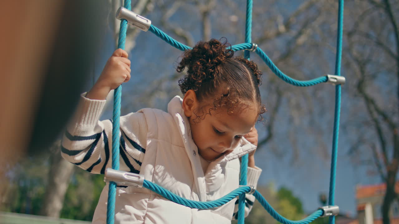 Child playing rope ladder sunny day close up. Girl climbing.
