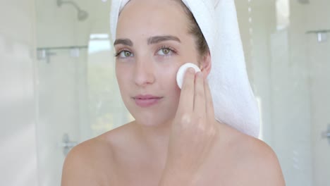 Portrait-of-happy-caucasian-woman-washing-her-face-with-cotton-pad-in-bathroom-in-slow-motion