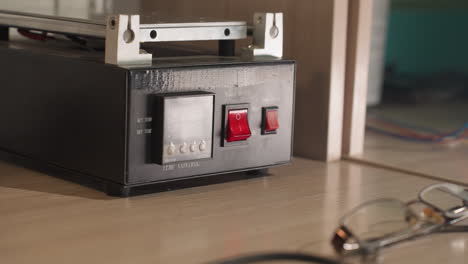 una vista de cerca de un técnico con guantes negros presionando un interruptor de energía rojo en un dispositivo de control de temperatura
