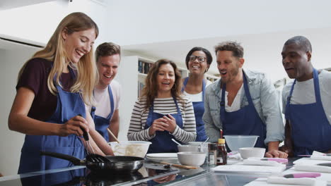 female teacher making flatbread on cooker in cookery class as adult students look on