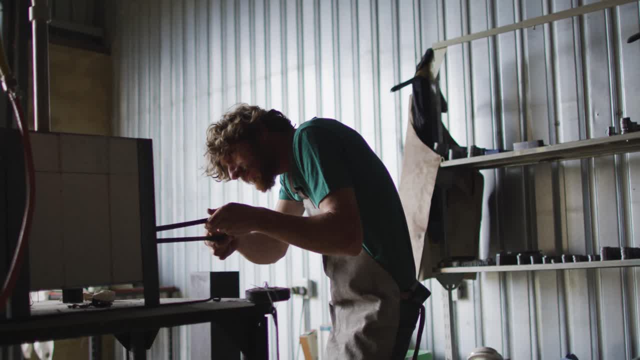 Caucasian male blacksmith holding hot metal tool in kiln with tongs in workshop