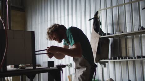 caucasian male blacksmith holding hot metal tool in kiln with tongs in workshop