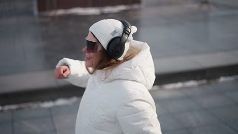 shoulder level view of dancer turning in smooth dance moves on icy pavement in snowy urban park with wind slipping through hair, capturing motion and vibrant energy against winter backdrop