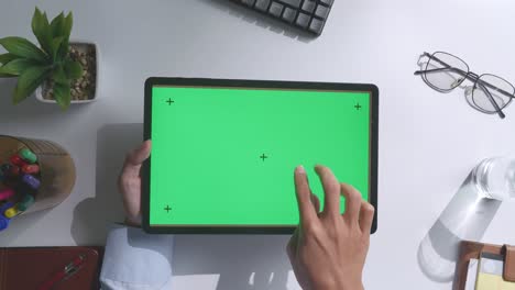 vista de arriba hacia abajo de una computadora portátil con pantalla verde simulada pantalla chromakey en un escritorio de oficina de madera al lado de la libreta con bolígrafos, gafas y un vaso de agua.