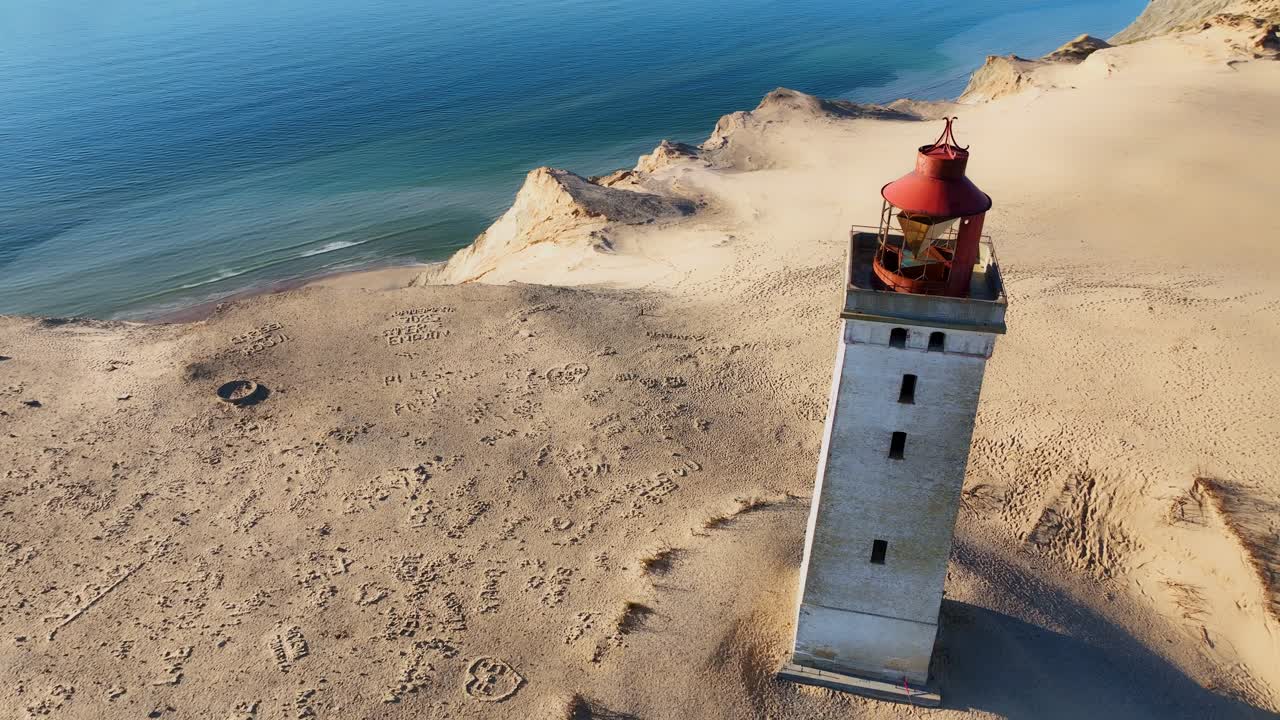 A close drone view captures Denmark’s iconic stone lighthouse as it stands proudly atop sweeping sand dunes, blending historic architecture with the raw beauty of the coastal landscape.