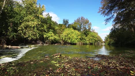 Water-flowing-over-a-large-rock-creek-bed,-lots-of-moss-in-foreground-and-trees-in-background