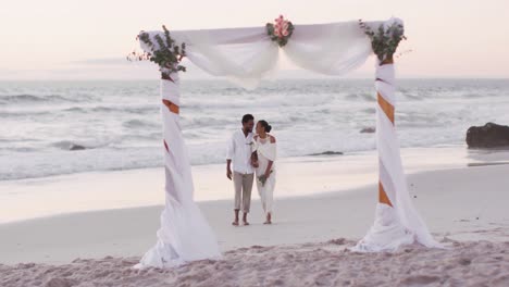 african american couple in love getting married, holding hands and walking on the beach