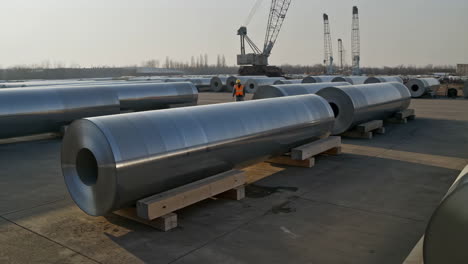 Large Metal Coils Stored in an Industrial Yard with a Worker and Cranes